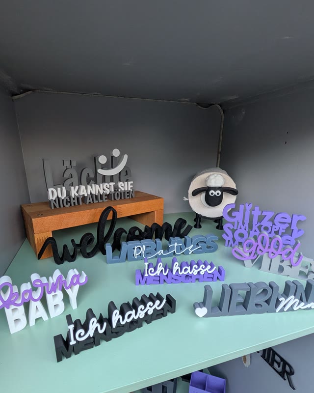 Schriftzüge „welcome“, „hallo Baby“ und „Ich hasse Plastik“ neben einem Schaf auf Holzsockel